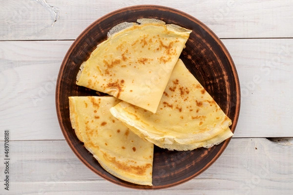 Fototapeta Several fragrant homemade pancakes on a ceramic plate on a wooden table, close-up, top view.