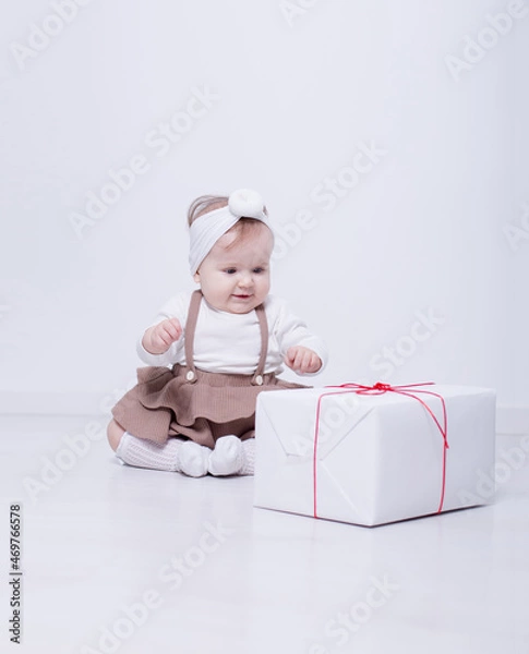 Obraz A beautiful, elegant girl received a gift. In a bright studio, a child plays and opens a gift..A picture of baby girl with big gift box