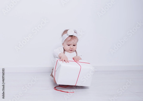 Obraz A beautiful, elegant girl received a gift. In a bright studio, a child plays and opens a gift..A picture of baby girl with big gift box
