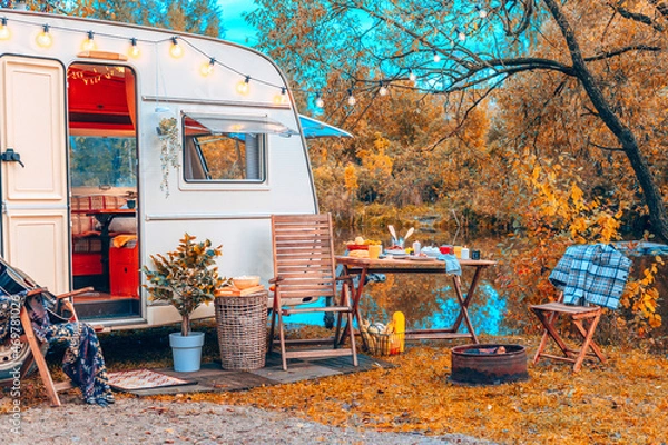 Fototapeta trailer of mobile home or recreational vehicle stands on shore of pond in camping in autumn near table set, concept of family local travel in native country on caravan or camper van and camping life