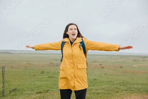 Fototapeta Woman outside in the dune landscape. Tourist in a yellow rain jacket holds her arms wide open as if she is flying. Vacation on the North Sea. Feeling of freedom and happiness while traveling