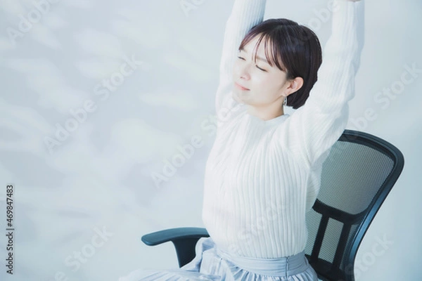 Obraz オフィスワークで肩こり・首こりを休憩時間に腕を伸ばしストレッチする女性