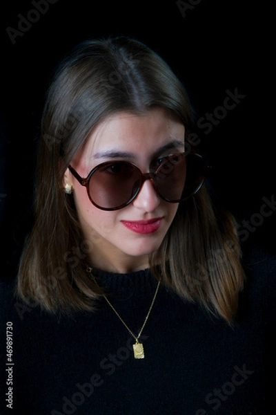 Obraz Stylish brunette woman wearing sunglasses on a dark isolated background.