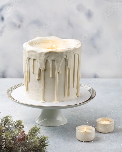 Fototapeta Сake in the shape of a candle. Christmas white cake on a white background with a Christmas decoration, lights or winter holidays pastry food concept.