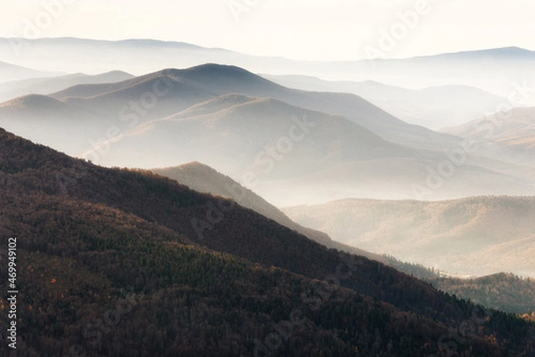 Fototapeta Beautiful landscape of autumn mountains layers range at  hazy morning. A view of the misty slopes of the mountains in the distance and forest hills  in rays of sunlight.Travel nature background.
