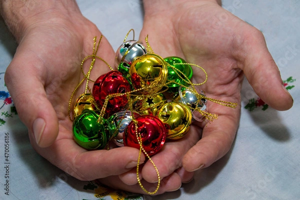 Fototapeta Multi-colored jingle bells in men's hands. Selective focus. On a light background. Close-up