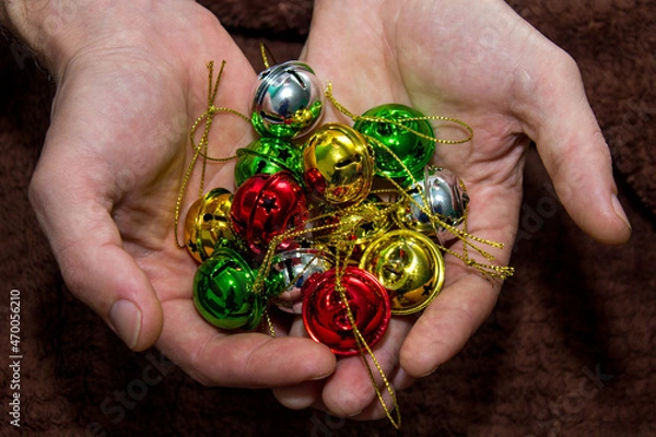 Fototapeta Multi-colored jingle bells in men's hands. Selective focus. Dark background. Close-up