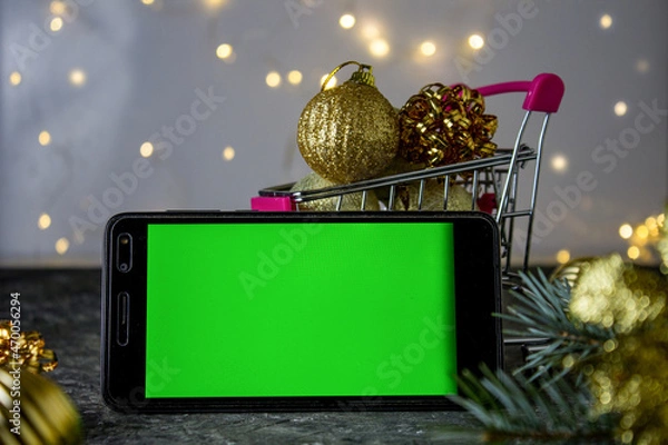 Fototapeta Mobile phone with chromakey on the background of Christmas decorations. Bokeh. Chromakey. Space for text