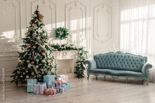 Fototapeta New Year's gifts in designer paper and bright ribbons under the Christmas tree on the floor on New Year's Eve. Christmas tree decorated with toys stands near the fireplace