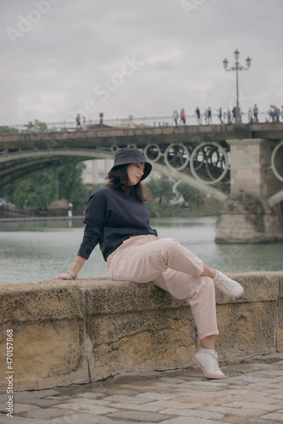 Obraz Caucasian girl sitting outdoors overlooking Isabel II bridge, Triana bridge.