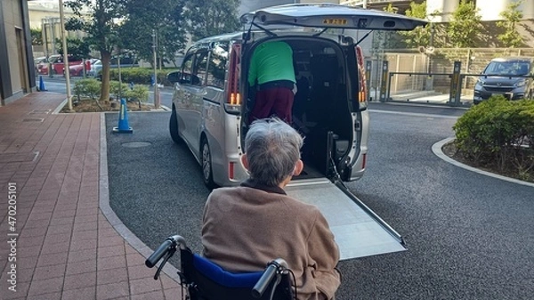 Obraz 車椅子に乗った老人男性を介助しながら福祉車両に乗せる介護施設職員