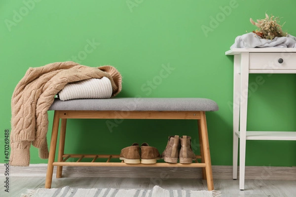 Obraz Stylish pouf with clothes and table near green wall