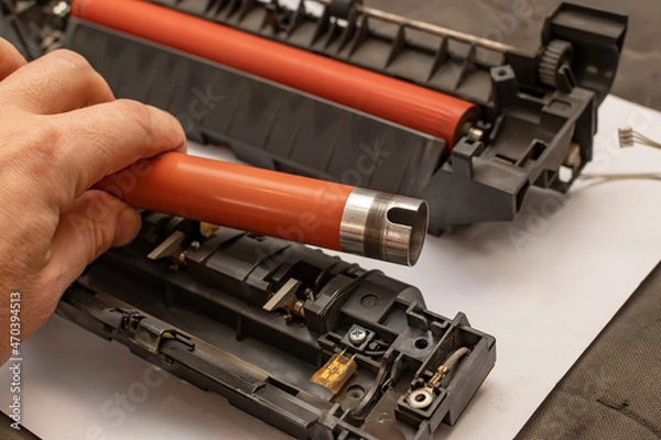 Fototapeta a view of a worn out upper heating shaft, roller from a printer in the hand of a person, a service center foreman who disassembles and repairs a thermoblock, a fuser from a printing office device