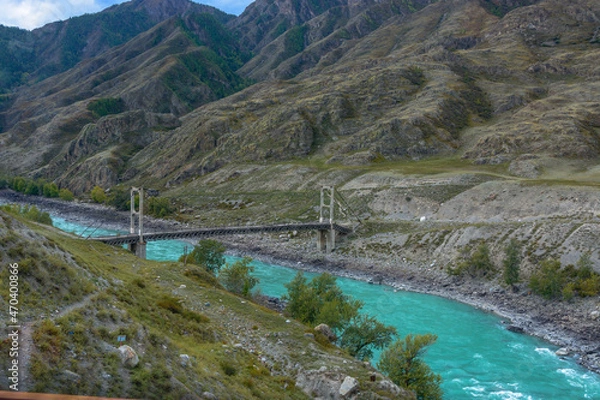 Fototapeta an old double-chain bridge with pylons across the river in a mountain valley in autumn. fuzzy focus
