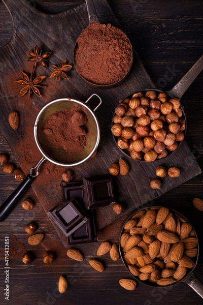 Fototapeta Still life. in the foreground with top view, vintage metal measuring spoons with shelled hazelnuts and almonds, cocoa powder, pieces of dark chocolate and star anise stars