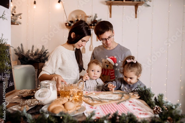 Obraz Beautiful family preparing homemade cakes on the christmas table against the backdrop of the decorations for the holiday