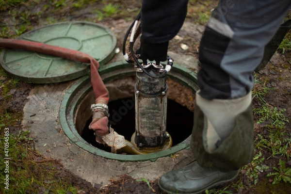 Obraz Sewer repair. The worker lowers the equipment into the sewer hatch.