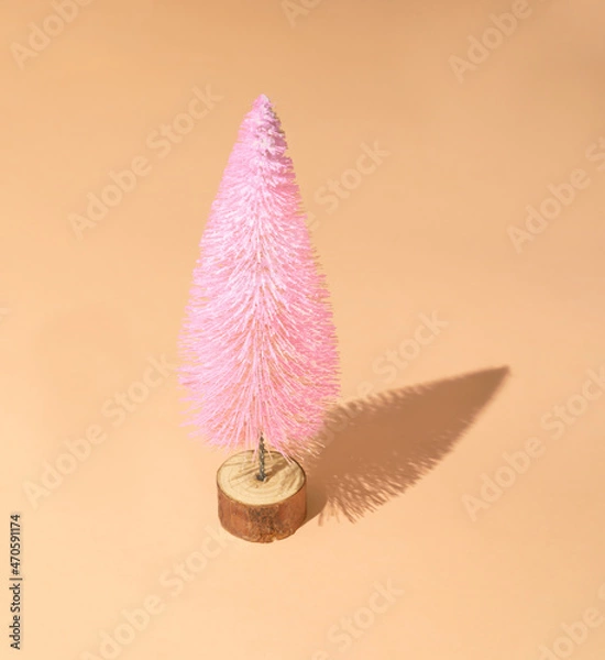 Fototapeta Christmas tree in rose pink colour with snow against peachy pastel background with sunny shadow. Minimal winter holidays and New Year layout.