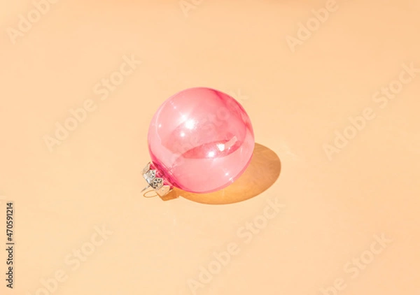 Fototapeta Christmas shiny pastel pink bauble against peachy pastel background with sunny shadow. Minimal winter holidays and New Year idea.