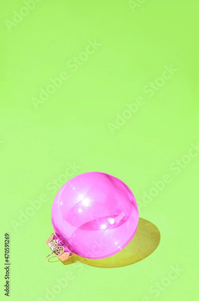 Fototapeta Christmas shiny violet bauble against vibrant pastel green background. Minimal winter holidays and New Year idea with ornament.