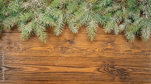 Fototapeta Spruce branches on a wooden textured background. Christmas banner with snow-covered branches of blue spruce lying on a rough wooden table. Christmas design template with copy space.