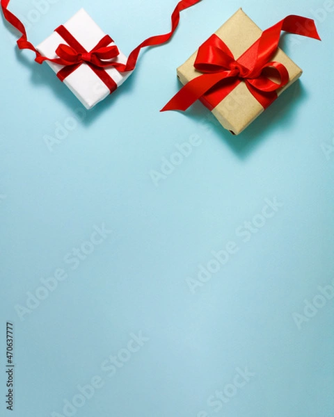 Fototapeta Two white brown paper gift boxes with a red satin ribbon bow and happy birthday sign on top on blue background. Christmas holiday mother and father Valentines days flat lay concept with copy space.