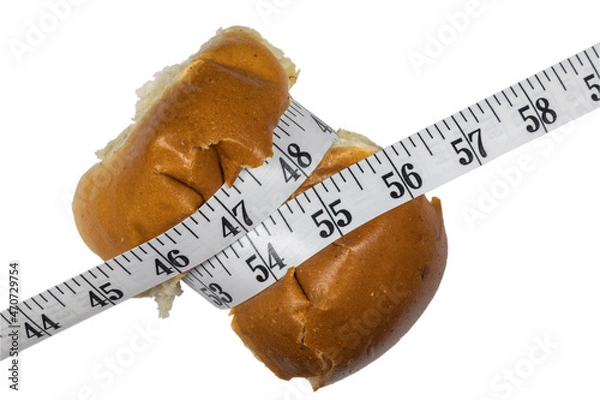 Obraz Bun compressed with measuring tape. The concept of willpower when losing weight. Weight and diet control. Bun on white background.
