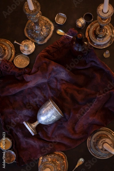 Obraz Flat lay view of tipped over silver chalice goblet grail surrounded by vintage candlesticks and miscellaneous vintage metal valuables