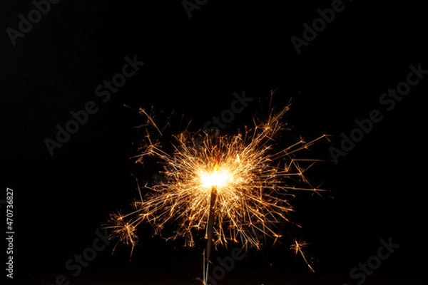 Fototapeta Horizontal conceptual close-up picture of an orange sparkler in action with lots of bright hot sparks flying in all directions on the black background