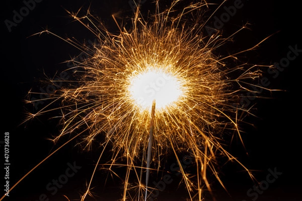 Fototapeta Horizontal dreamy close-up picture of a golden sparkler making many small shiny and hot sparkles on the black background