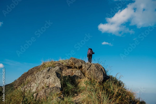 Fototapeta hiking girl standing with his back on the top of a tall rock beautiful blue sky