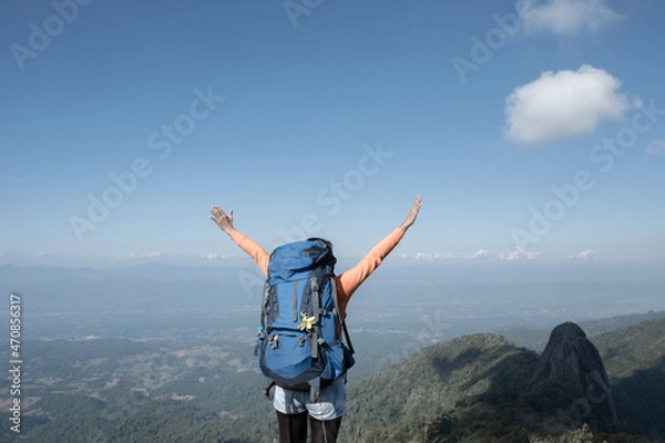 Fototapeta A trekker extends his arms on top of the mountain.