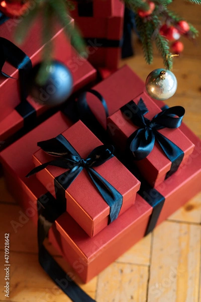 Obraz Christmas gifts under a snowy tree, beautiful red boxes. Gift for the new year. Beautiful box with a bow. Dark background.