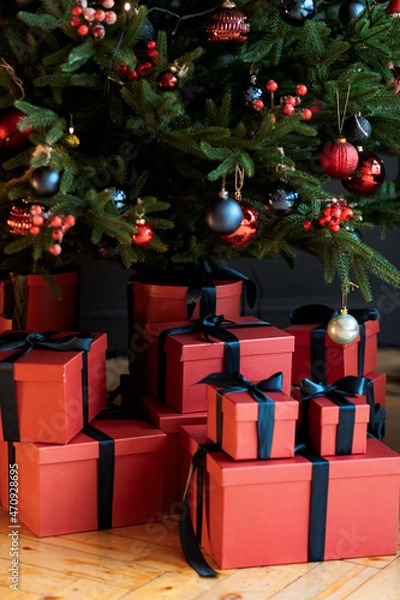 Obraz Christmas gifts under a snowy tree, beautiful red boxes. Gift for the new year. Beautiful box with a bow. Dark background.