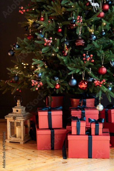 Obraz Christmas gifts under a snowy tree, beautiful red boxes. Gift for the new year. Beautiful box with a bow. Dark background.