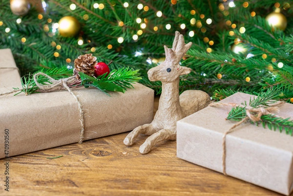 Obraz Christmas eco-friendly gifts wrapped in wrapping paper on a wooden table with fir branches and a garland. A papier-mache deer figurine. Selective focus. Close-up, copy space,concept Christmas