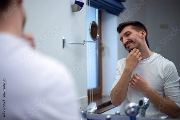 Obraz A guy with a patchy beard looks in the mirror