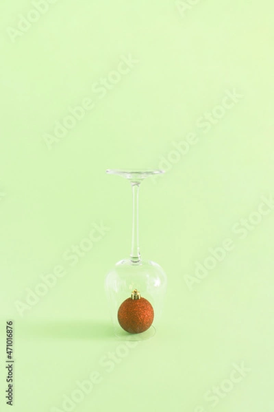 Obraz Christmas and New Year decoration idea with a drinking glass and red bauble on pastel bright green background. Creative holiday party and winter concept, minimal vertical aesthetic composition.