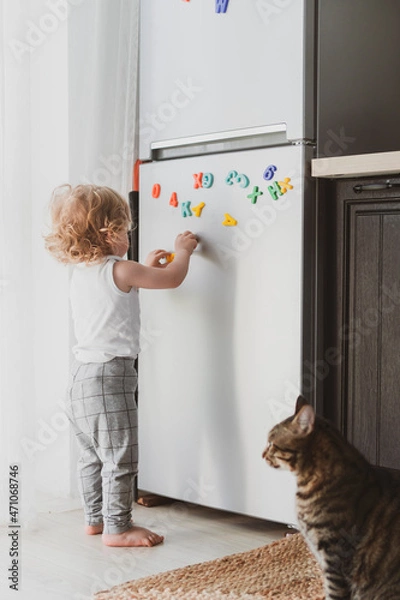 Obraz little cute toddler playing with toy letters on the fridge