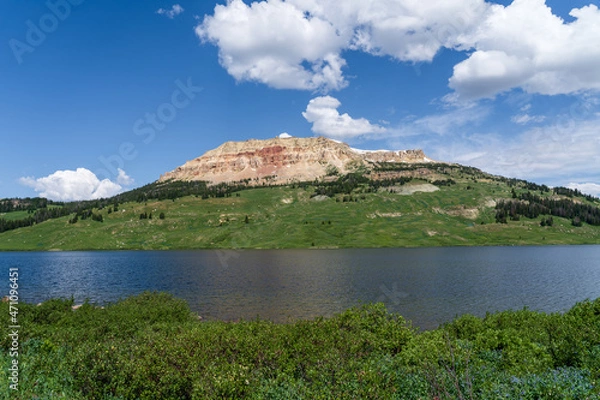 Fototapeta Beartooth Lake on a sunny summer day in the Beartooth Highway in the mountains of Wyoming and Montana - an alpine lake with a green and red rock mountain in the background