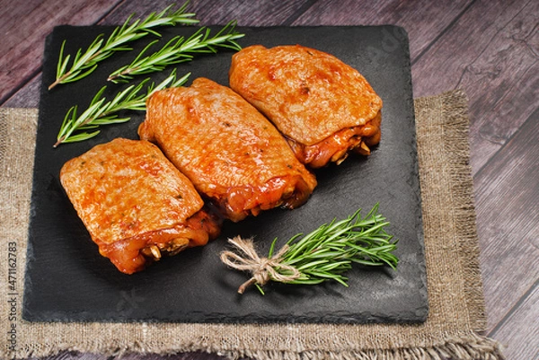 Obraz Raw chicken meat.Chicken thighs marinated in red sauce on a kitchen ceramic board with rosemary leaves.