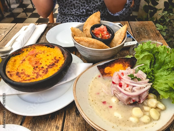 Obraz Date table with peruvian 'ceviche' (fresh raw fish cured in fresh citrus juices) in a plate, 'pastel de choclo' (corn cake) and 'empanadas' (fried turnover of pastry and filling)