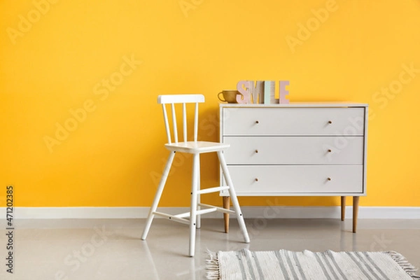 Fototapeta Modern chair and chest of drawers near color wall
