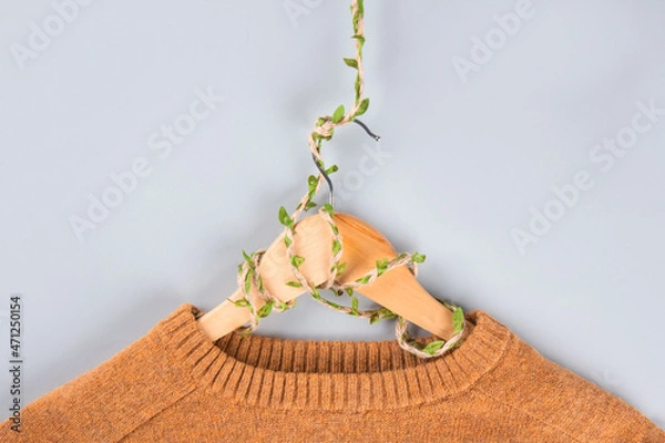 Fototapeta Orange sweater on hangers entwined with plants on gray background with copyspace. Conscious and environmentally friendly consupmtion - new modern trends in shopping. Zero waste. Slow fashion concept.