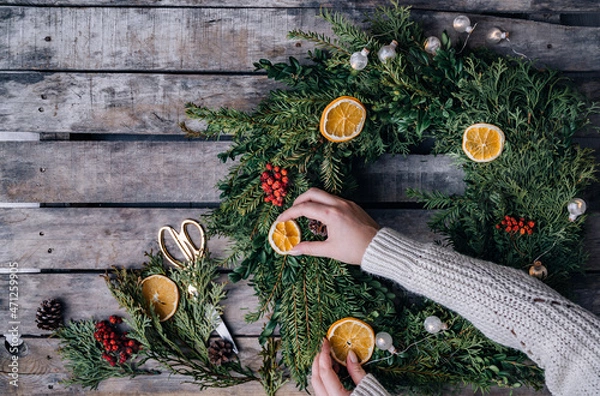 Fototapeta Top view of florist hands making Christmas wreath on wooden tabletop
