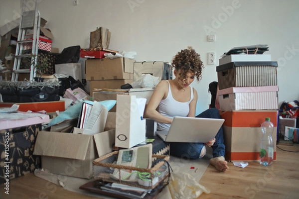 Fototapeta woman organizes boxes and works with pc during a move