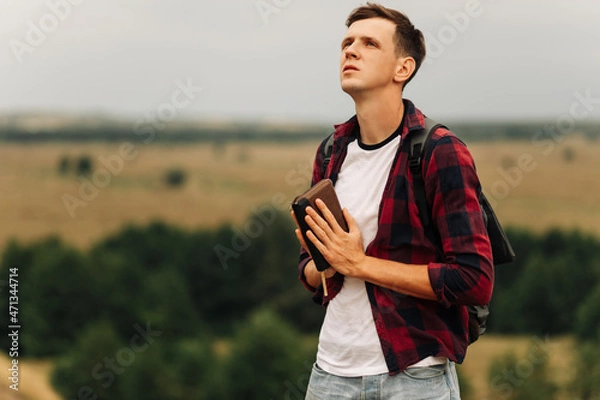 Fototapeta man closed his eyes, prayed in the open air, holding the Bible in his hands. holding a Bible in his hands