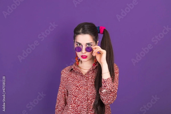 Fototapeta Portrait of cute young brunette dressed in 90s style on purple studio background.
