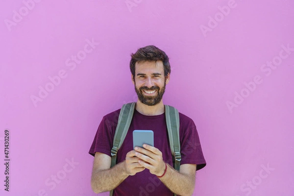 Fototapeta front view of caucasian man holding a phone on pink background. Horizontal view of latin american man using technology isolated on pink wall. People and travel concept.