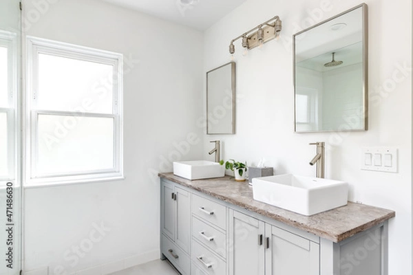 Fototapeta An elegant, renovated bathroom with white sinks, grey vanity, granite countertop, and bronze hardware, faucets and light. 